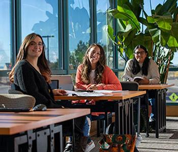 Three students sitting at study tables and smiling at camera