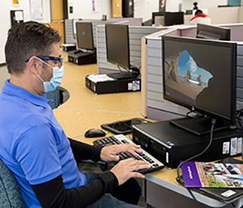 在计算机实验室里，学生坐在书桌前用笔记本电脑工作